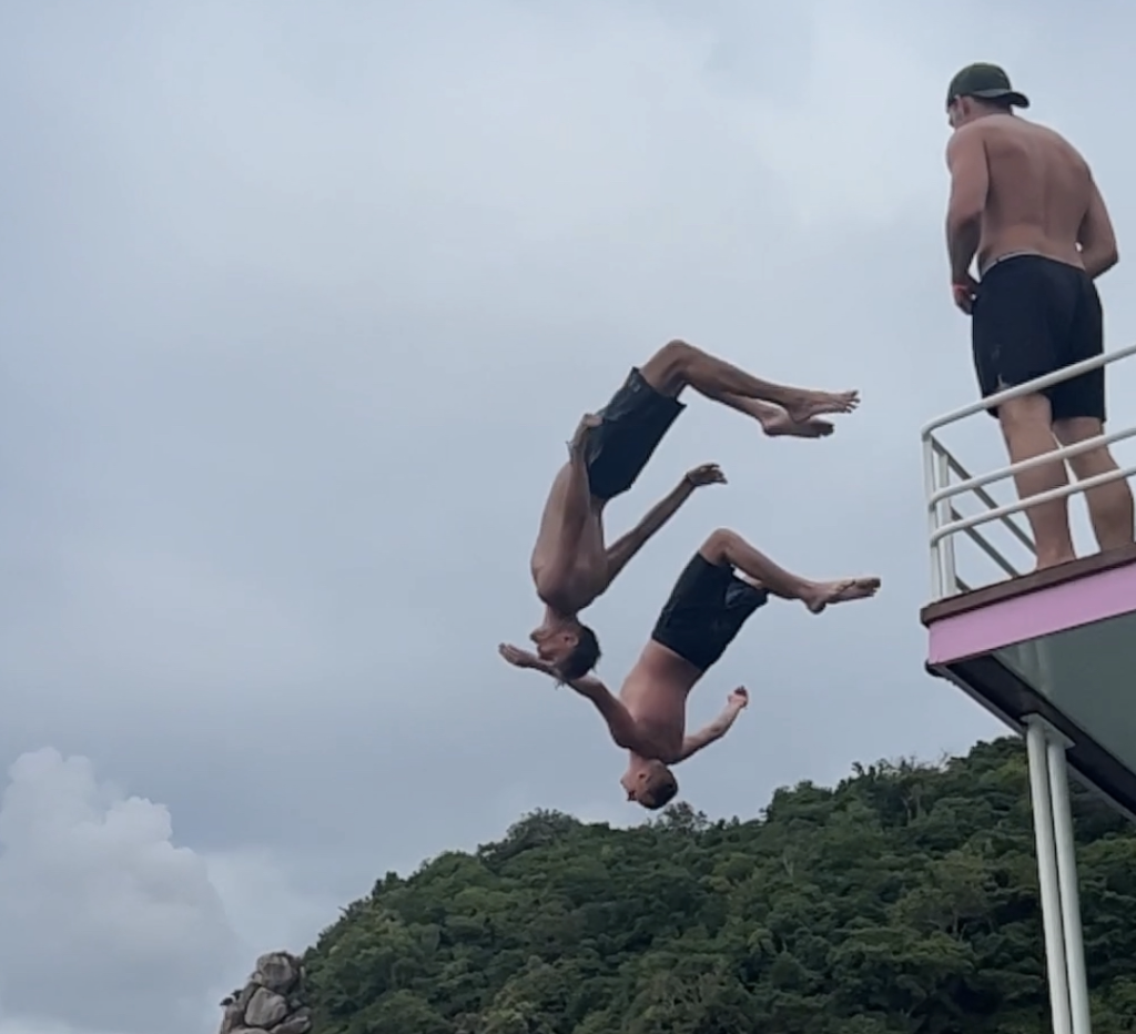 Two men do a backflip of a boat into the sea